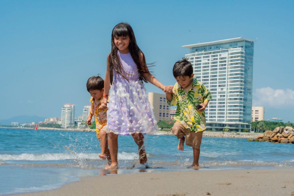 Three children running along the shore in front of a beachfront resort