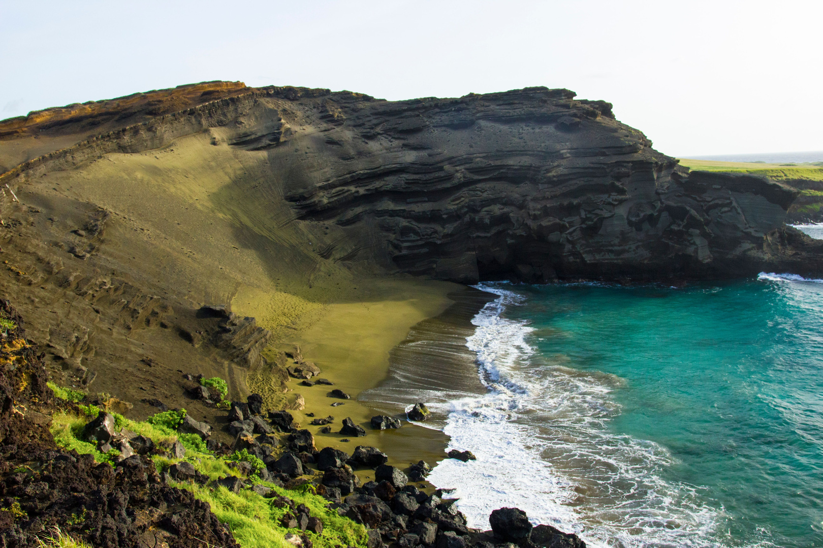 Green cliffs meeting a turquoise sea above black volcanic rock