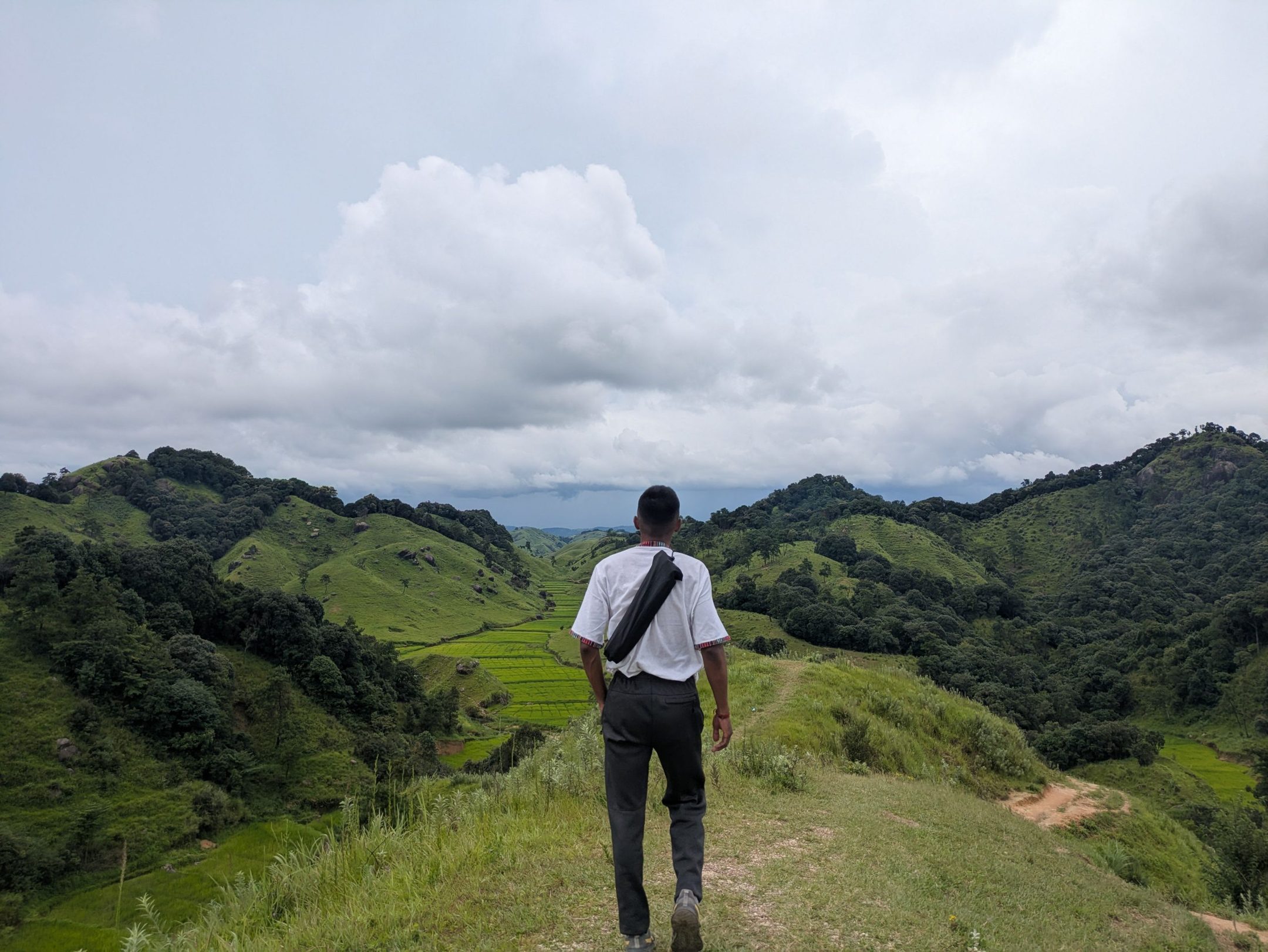 Man walking a ridge path over green hills under heavy cloud