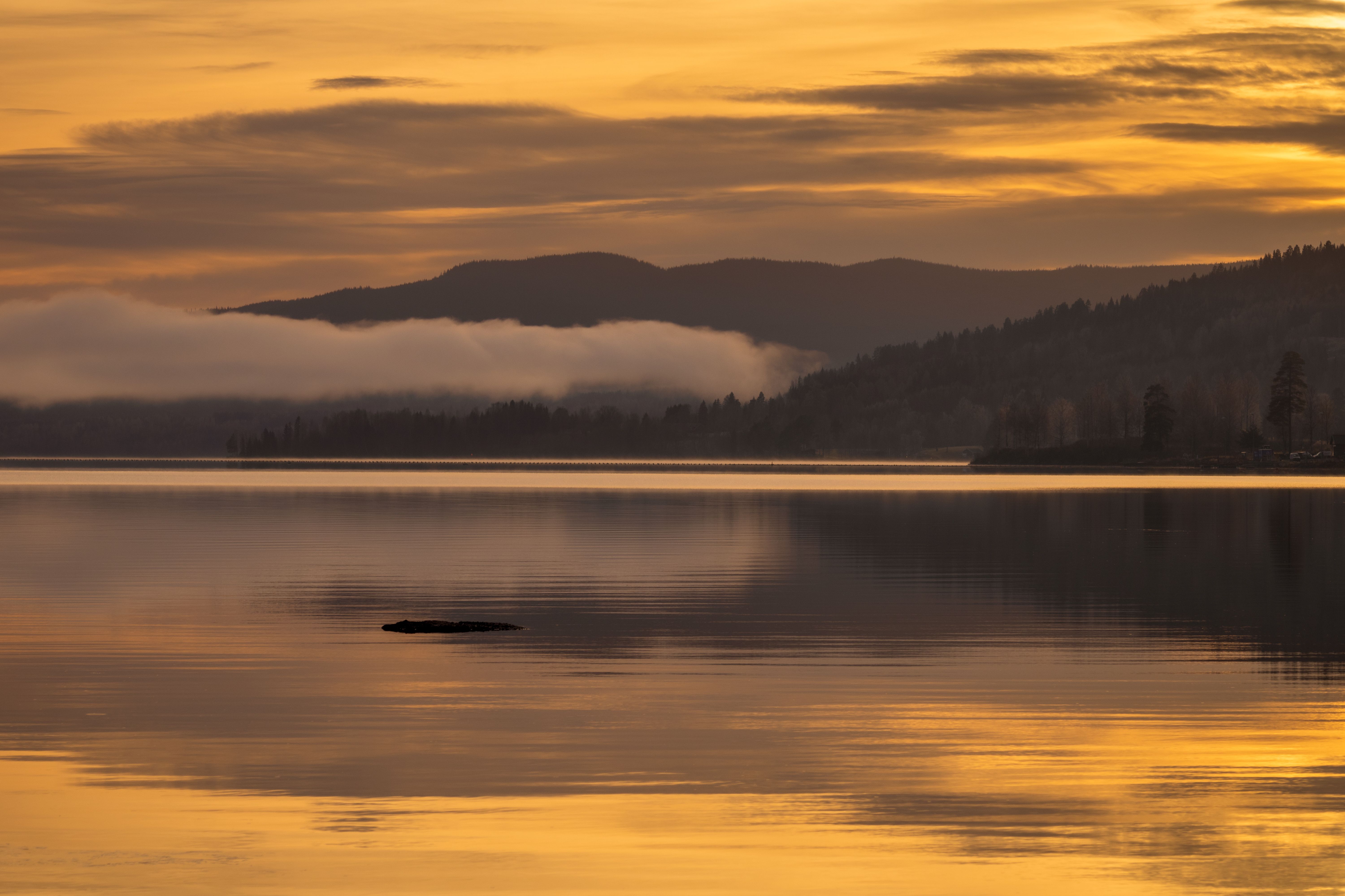 A still mountain lake at sunset, low hills and mist fading into gold