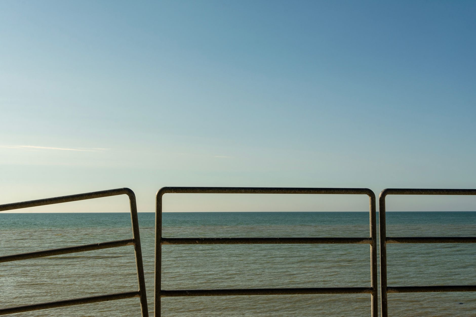 A calm sea horizon seen through a weathered railing