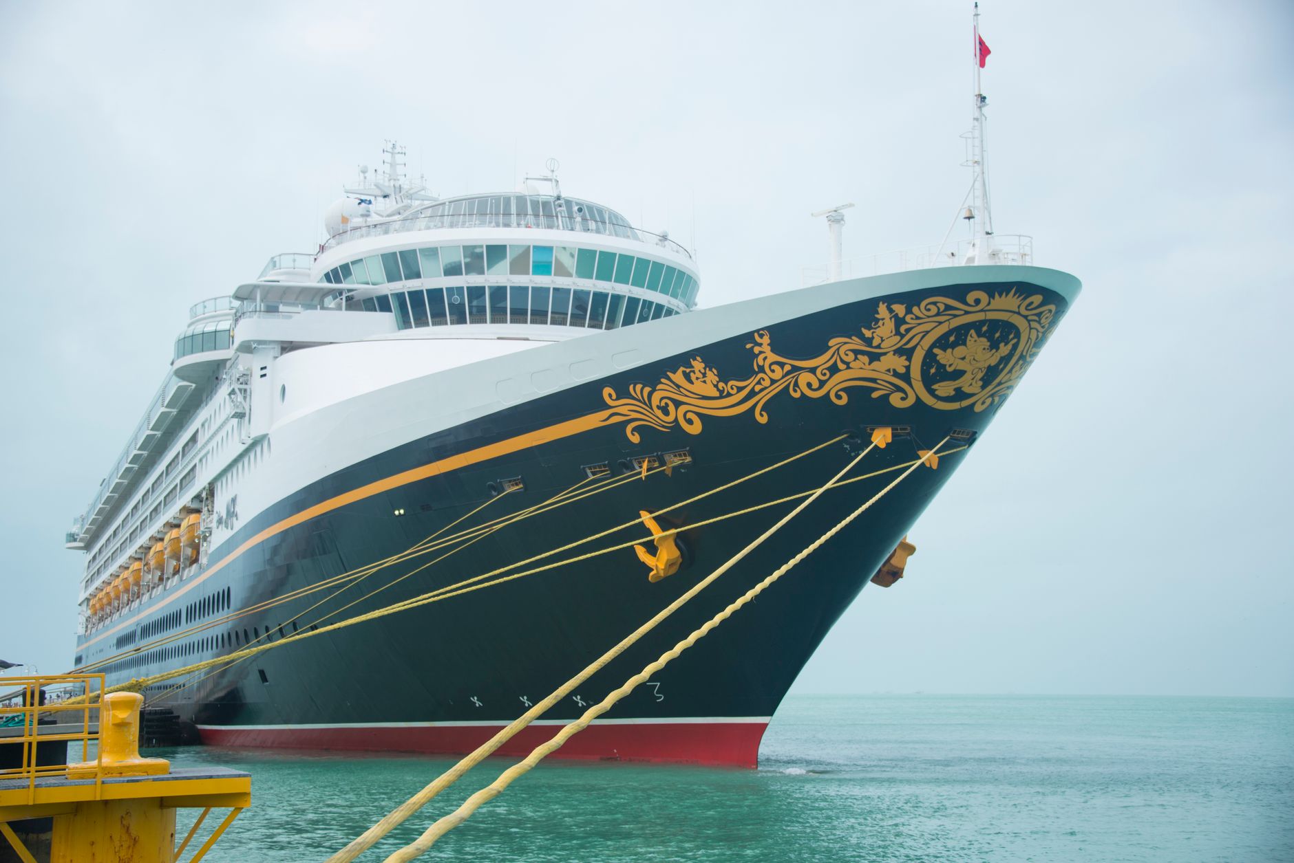 A large dark-hulled cruise ship with gold scrollwork docked at a pier under overcast skies