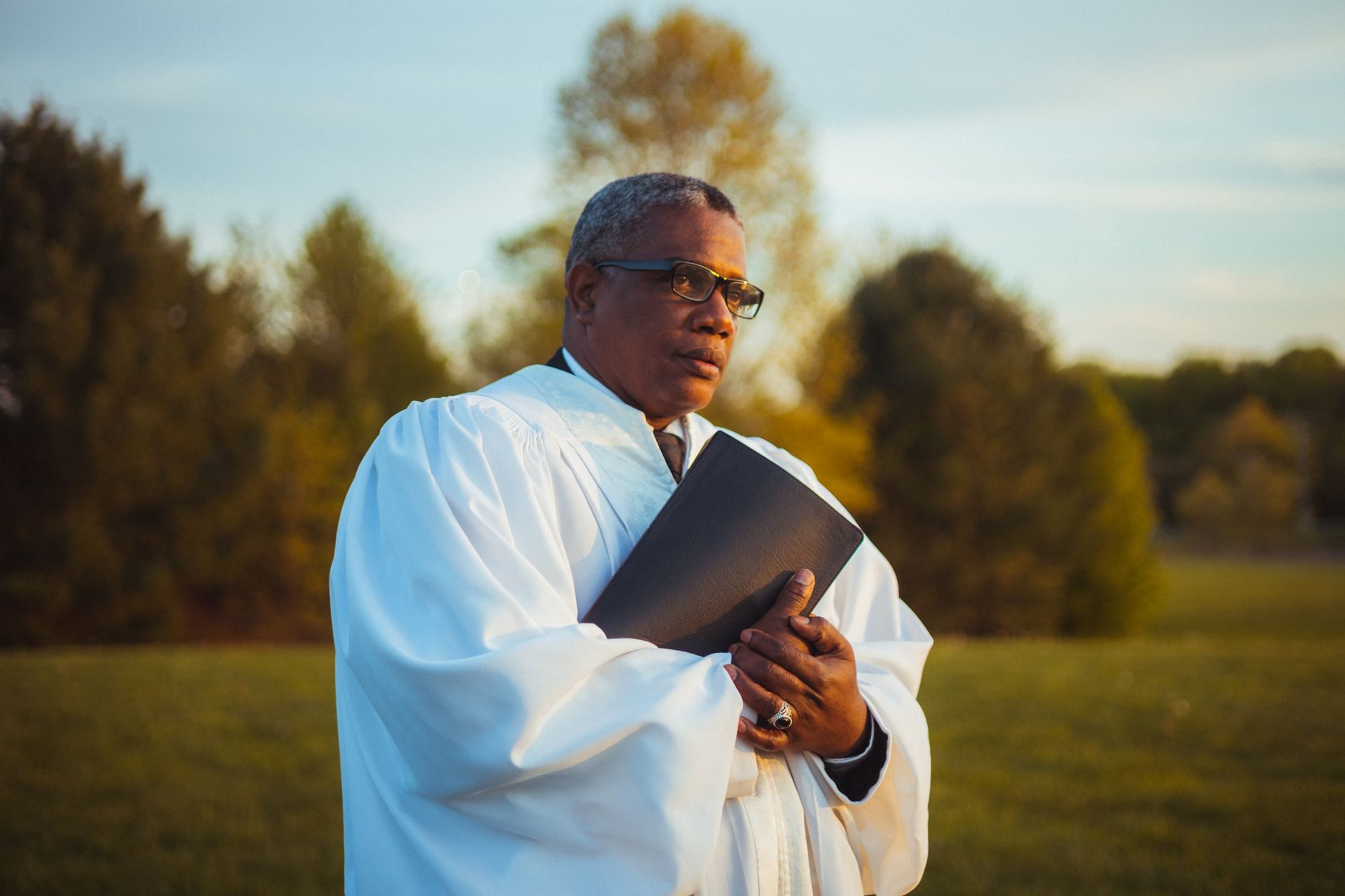A man in a white robe holds a book outdoors in warm golden light