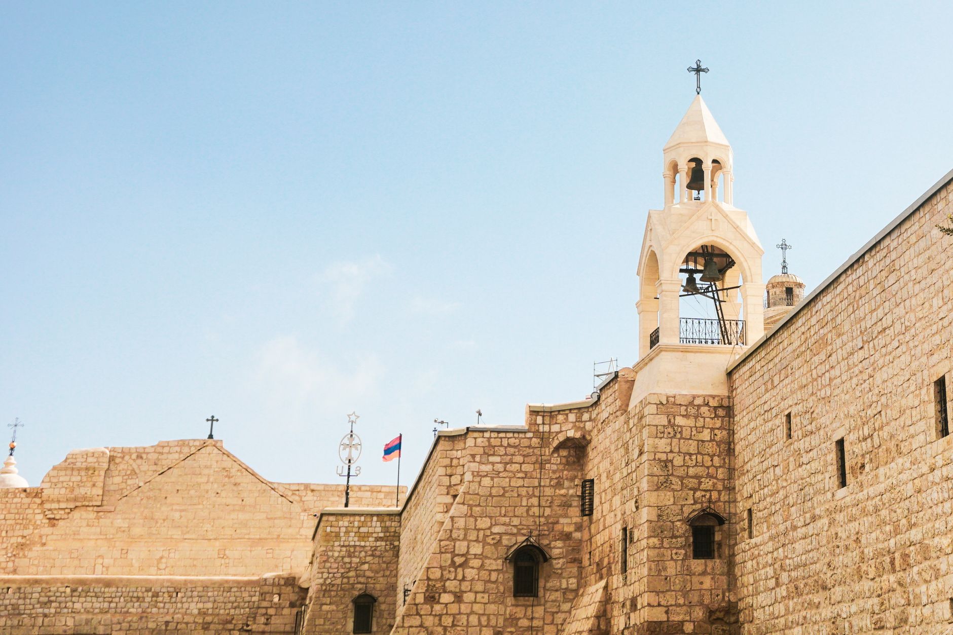 A stone church with a cross-topped bell tower rising above high fortified walls