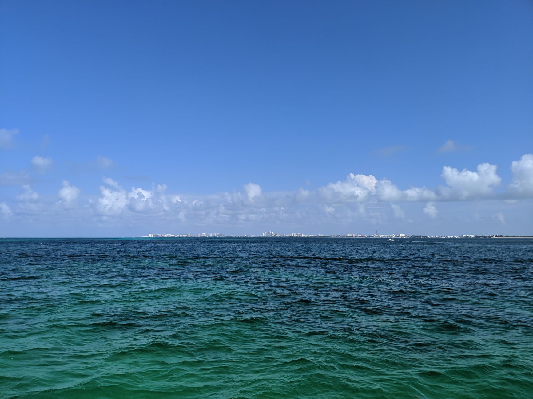 Deep open water under a wide cloudy sky, a low coastline on the far horizon