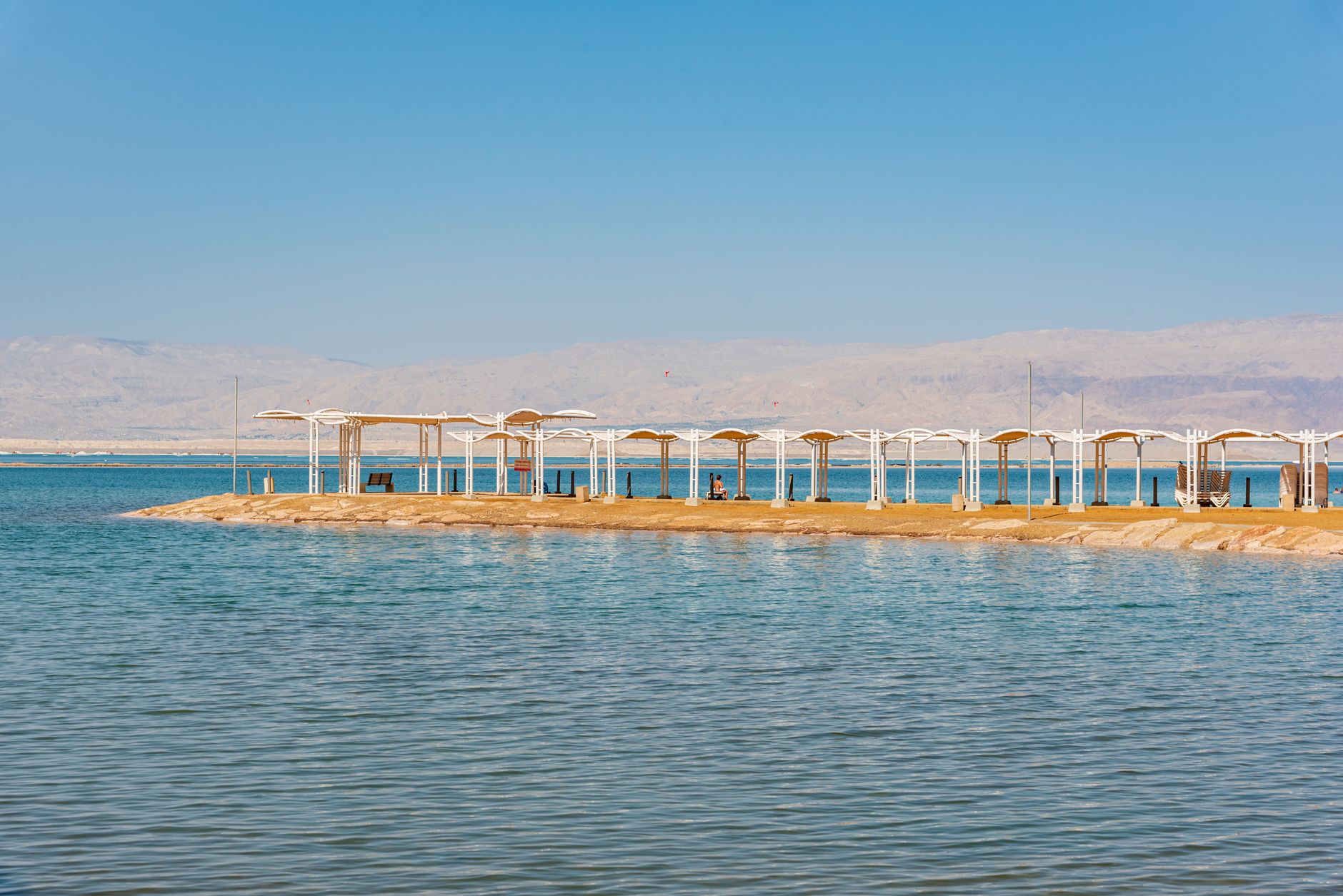 A white colonnaded walkway on a narrow spit reaching into still turquoise water