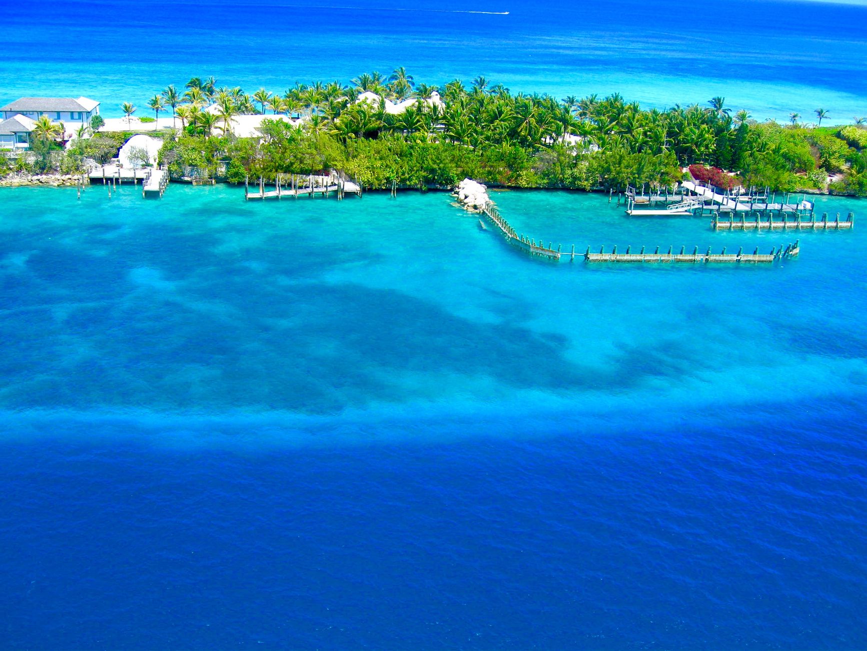 Aerial view of a small green island edged with jetties in turquoise water