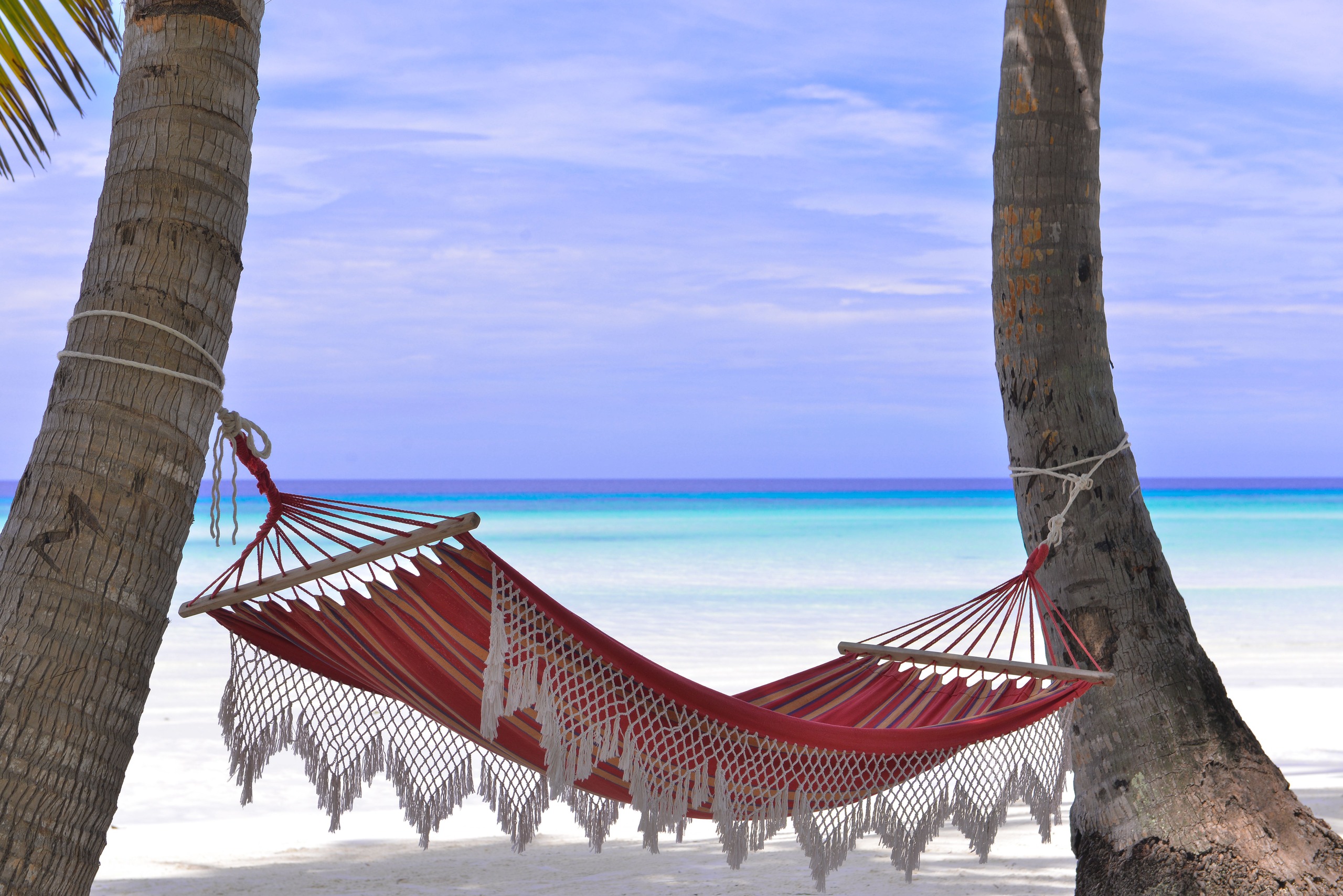 A hammock slung between two palms above the turquoise Caribbean at Riviera Maya