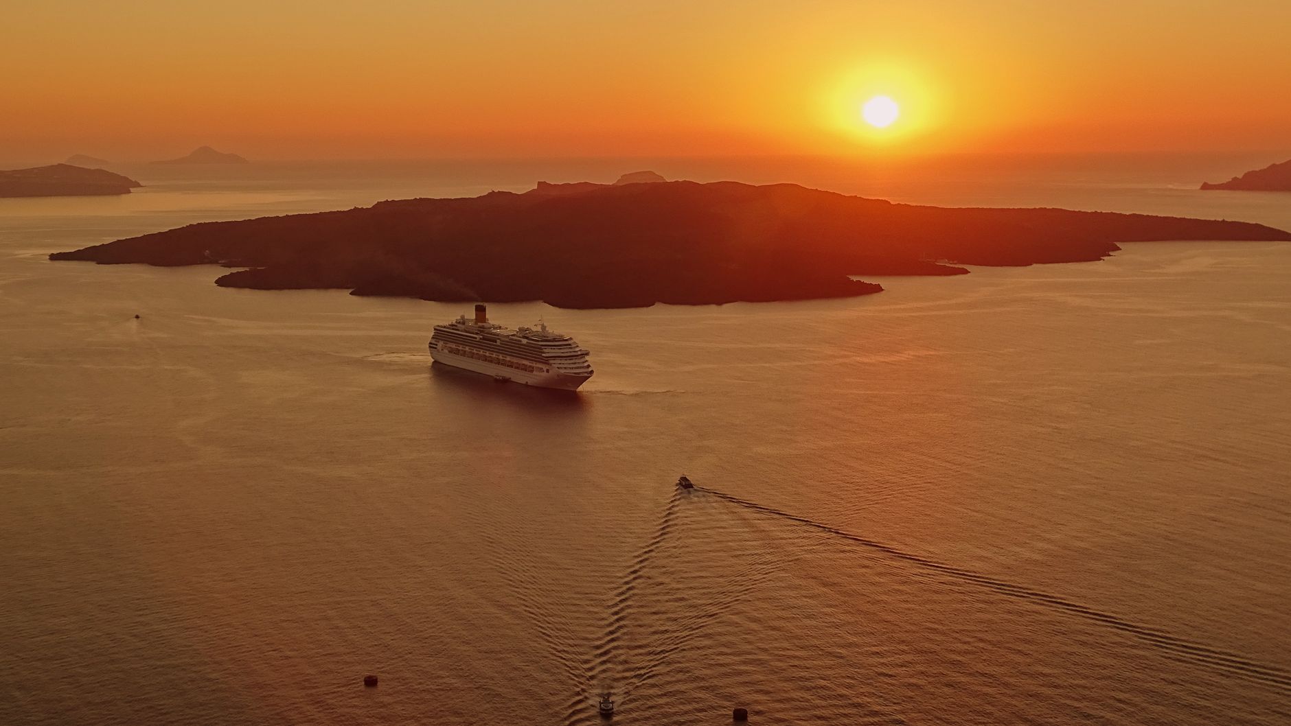 A cruise ship on a calm sea at sunset, a dark island silhouetted beyond