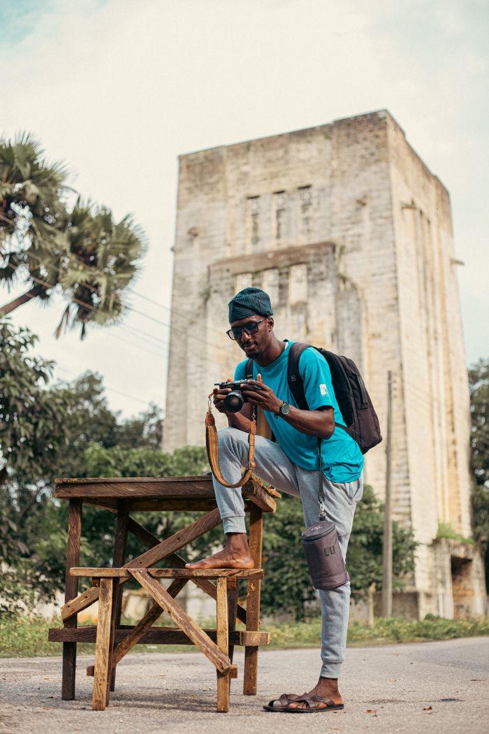 Photographer posing with camera near a historic tower outdoors.